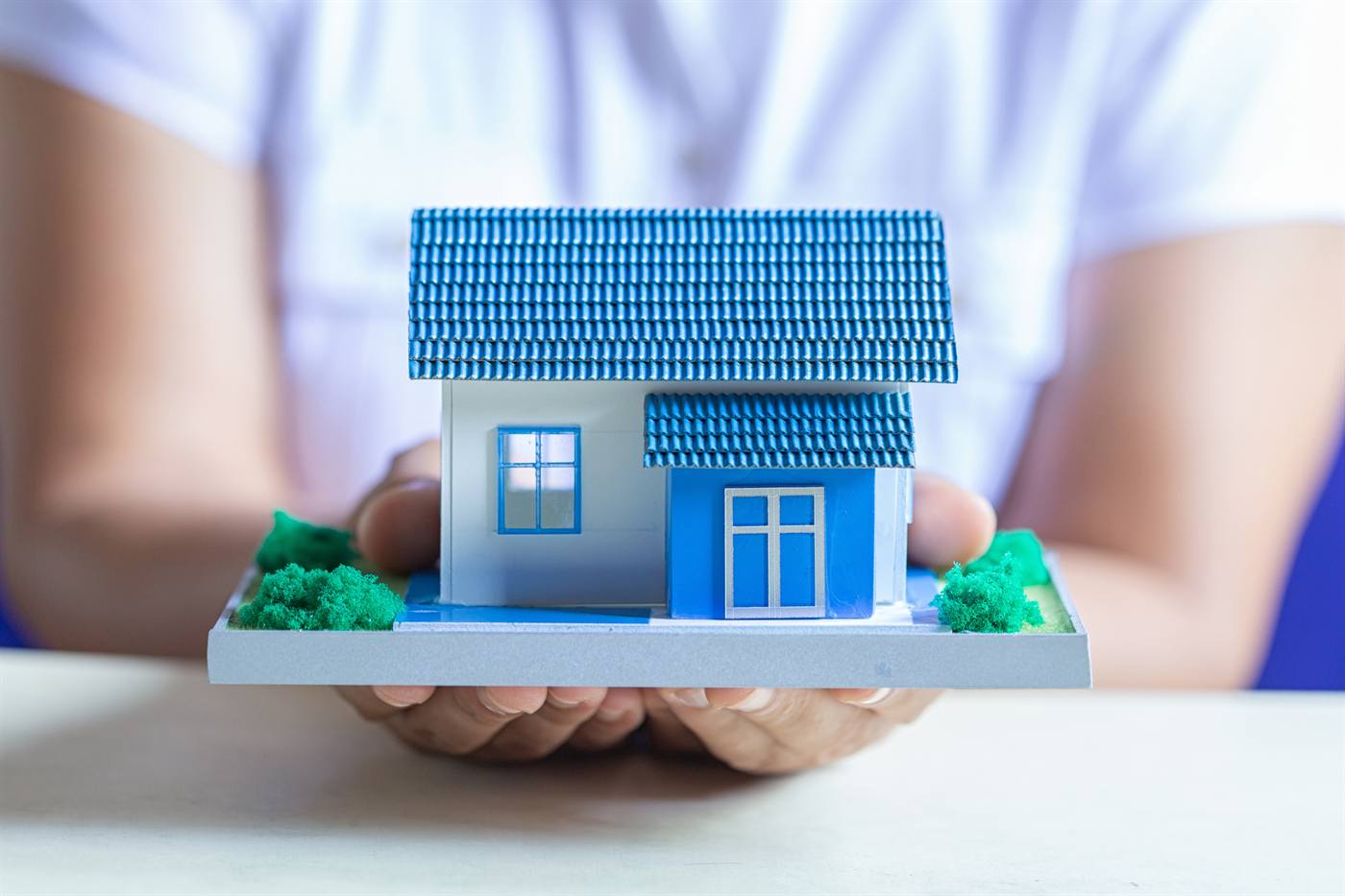 Hands holding a small house model for an as-is home sale